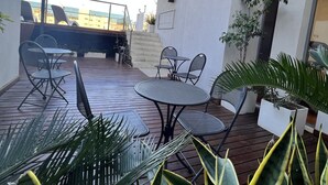 An outdoor patio with a wooden deck, metal chairs, a round table, and potted plants.