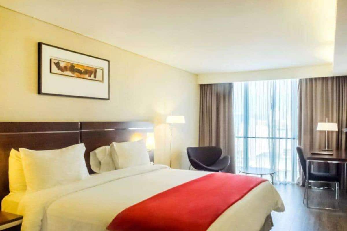 Una habitación de hotel con una cama grande, un escritorio, una silla y un ventanal con cortinas.