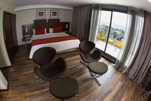 A hotel room with a large bed, two nightstands, a desk, and a balcony with yellow chairs. - Howard Johnson by Wyndham Córdoba La Cañada (Córdoba)