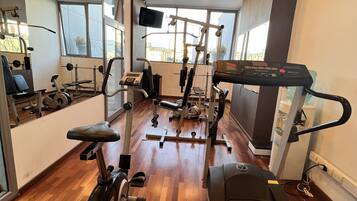 A gym with various exercise equipment, wooden flooring, and large windows providing natural light.