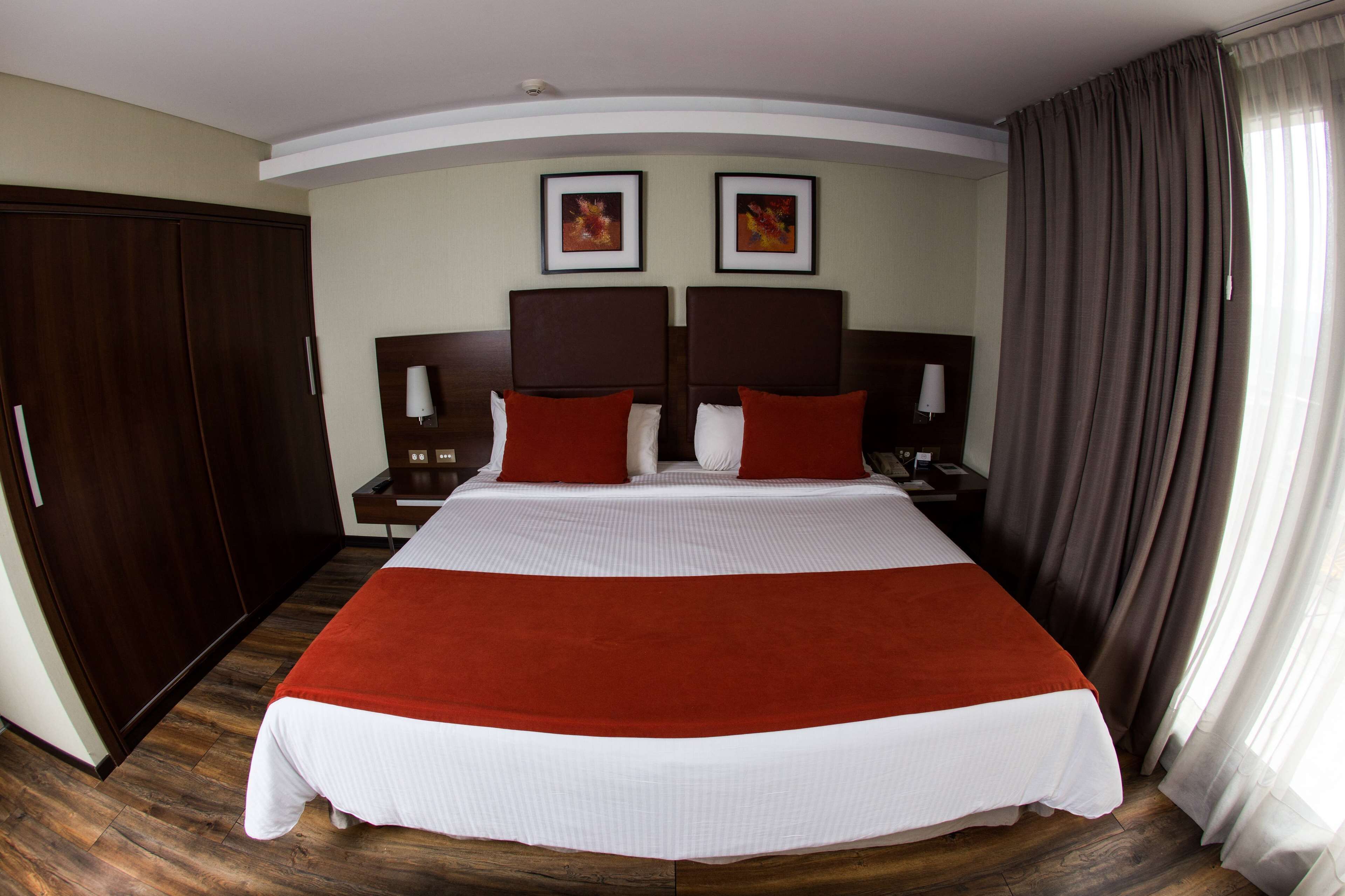 Un letto grande con una coperta a righe rosse e bianche, due comodini con lampade, un armadio in legno e due quadri appesi al muro.