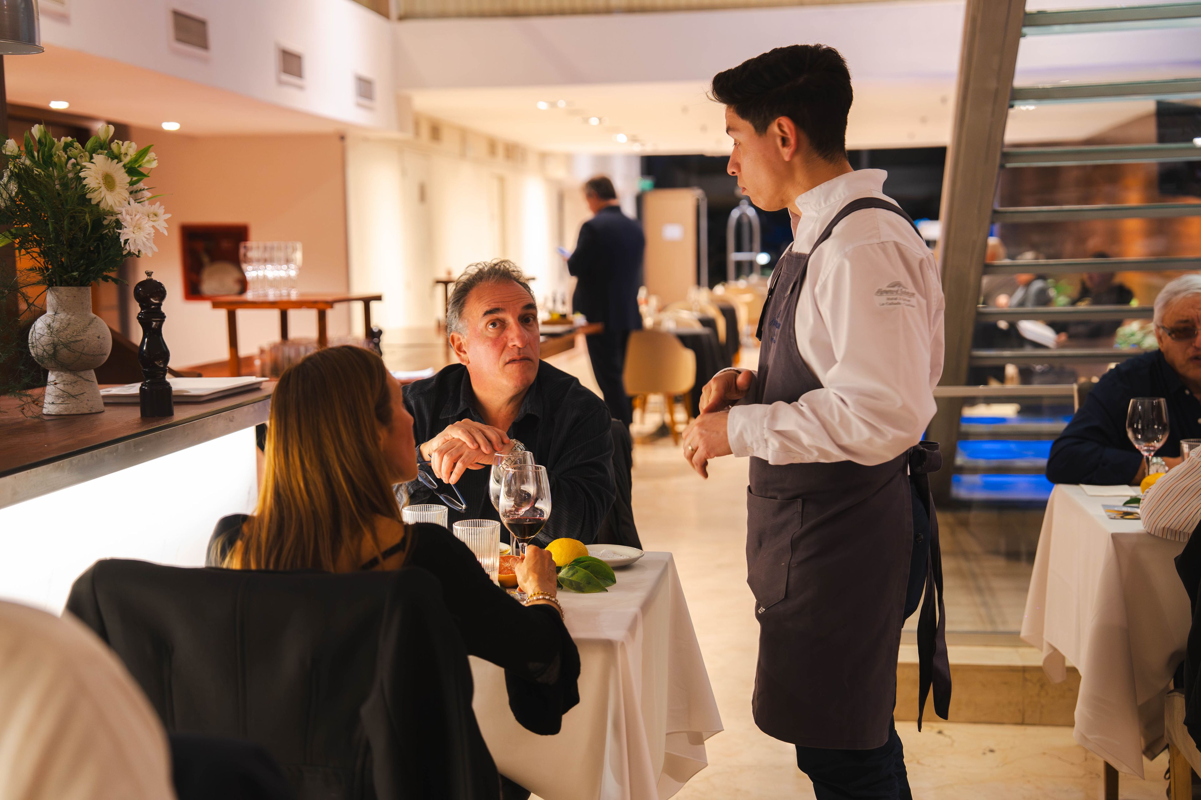 Interior de un restaurante con mesas, sillas y un camarero atendiendo a los clientes.