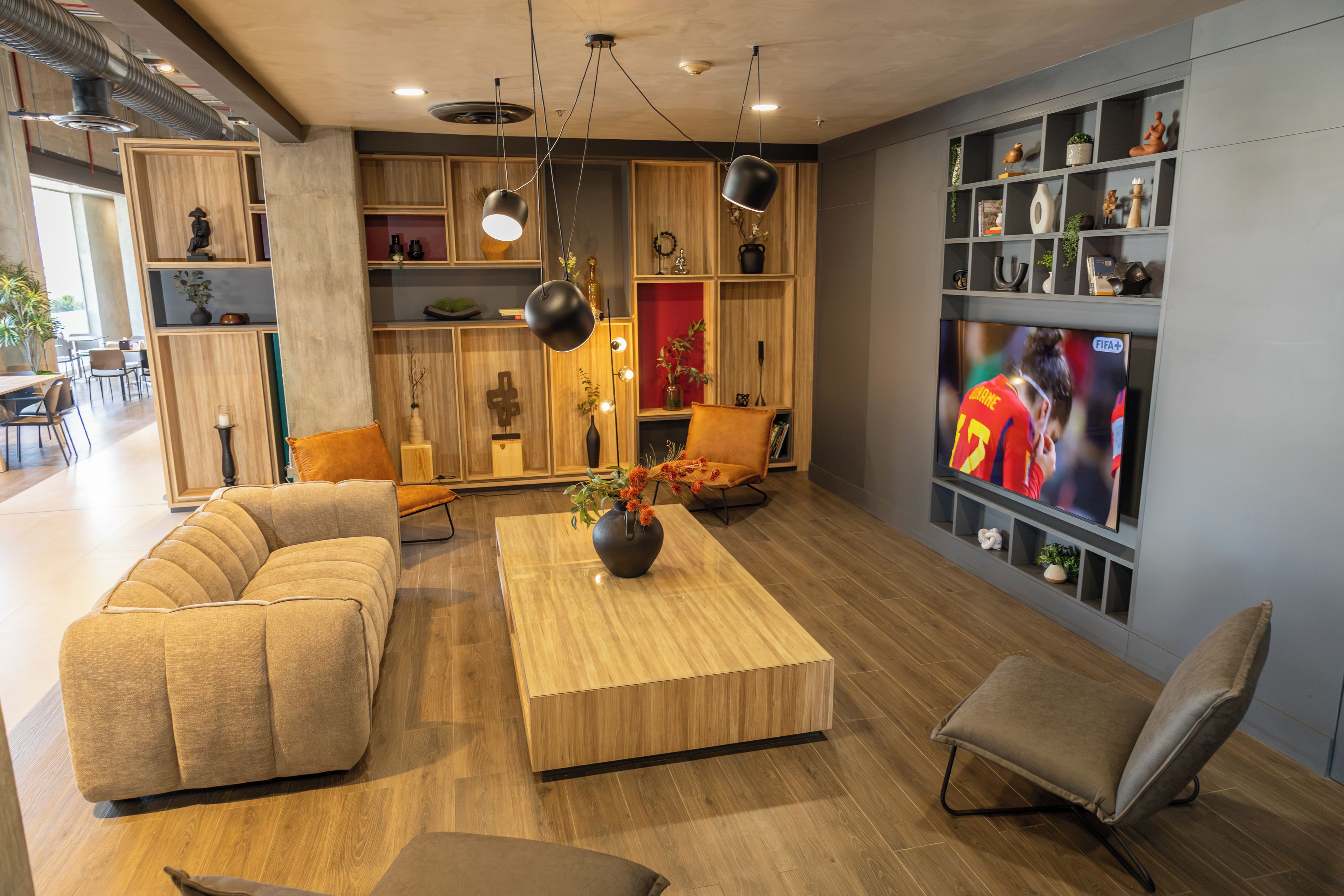 Una sala de estar moderna con un sofá, una mesa de centro y un televisor. Hay estanterías con adornos y una planta.