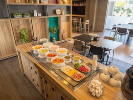 Um buffet de café da manhã com diversos alimentos e uma área de estar com mesas e cadeiras.