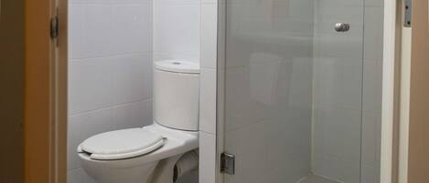 A bathroom with a toilet, a glass shower enclosure, and a tiled floor.