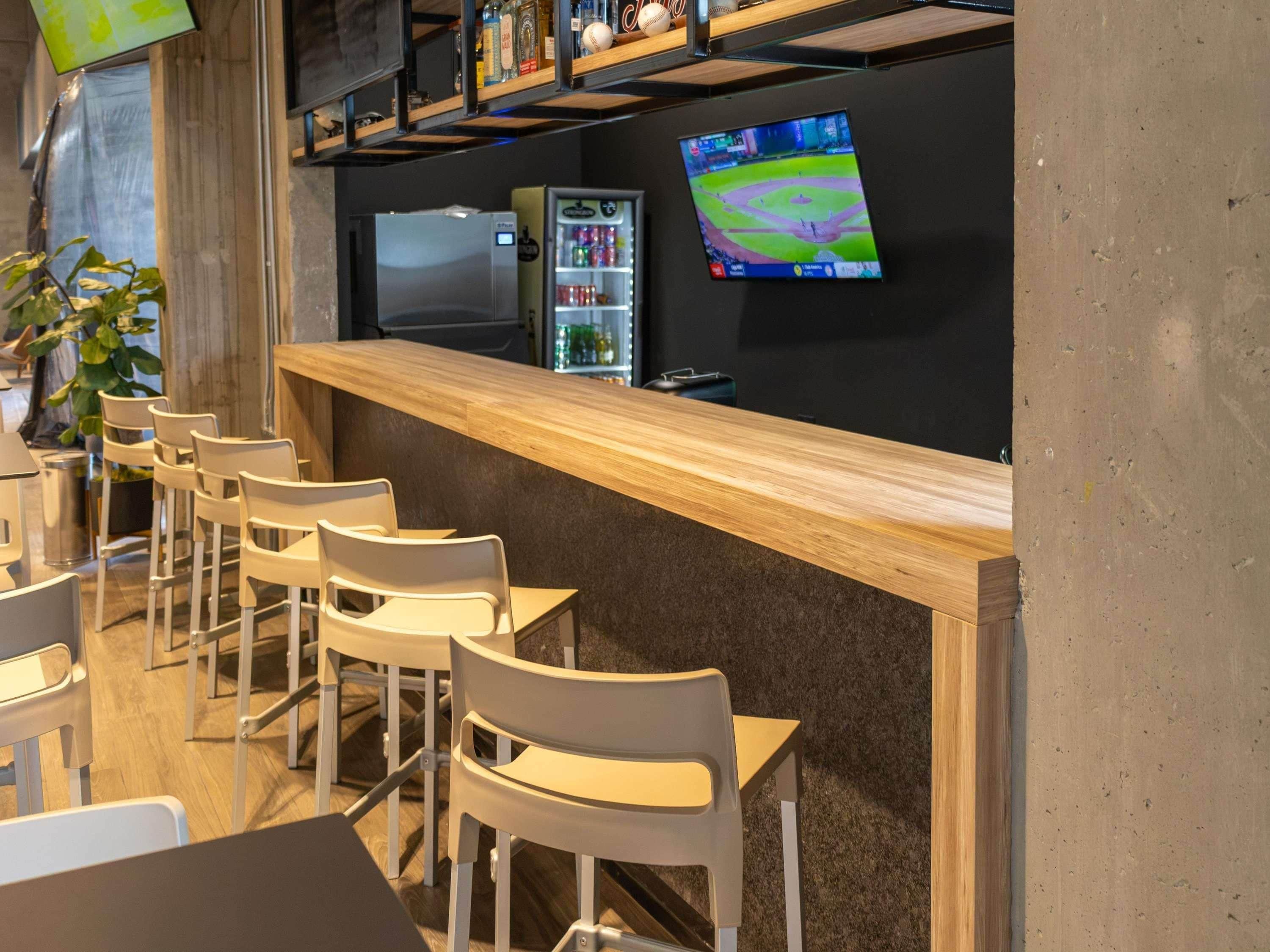 A bar area with a counter, chairs, a refrigerator, a television, and shelves with bottles.