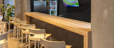 A bar area with a counter, chairs, a refrigerator, a television, and shelves with bottles.