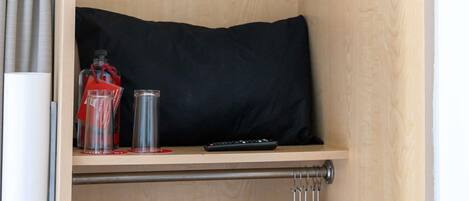 A wooden shelf with a black pillow, a remote control, and a glass bottle with a red tag.