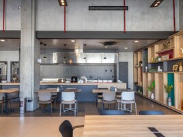 Ein modernes Restaurant im Inneren mit hohen Decken, freiliegenden Lüftungsrohren und einer zentralen Kochinsel mit Sitzgelegenheiten.