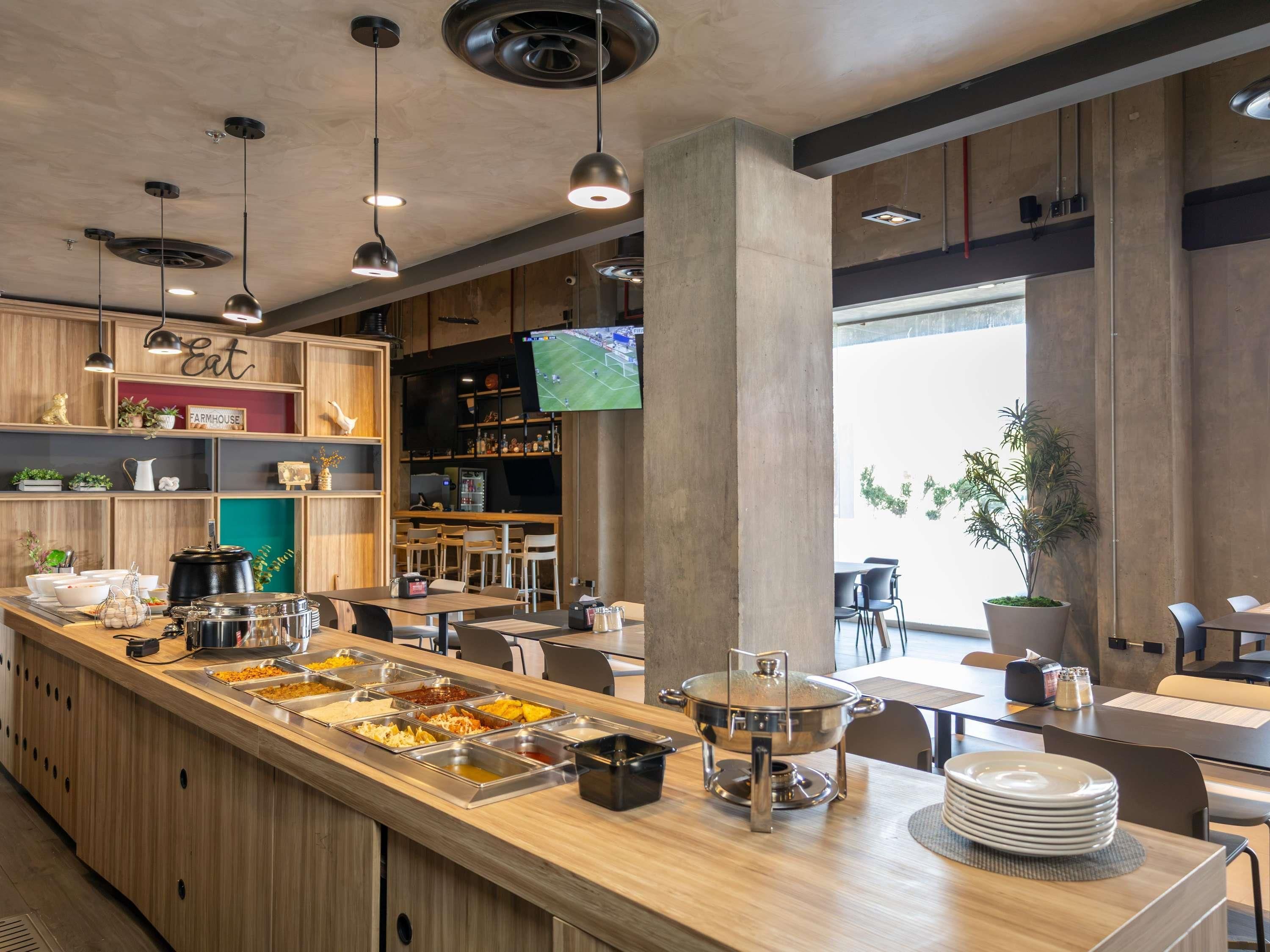 Una cafetería moderna con una barra larga, varias estaciones de comida y una pantalla de televisión.