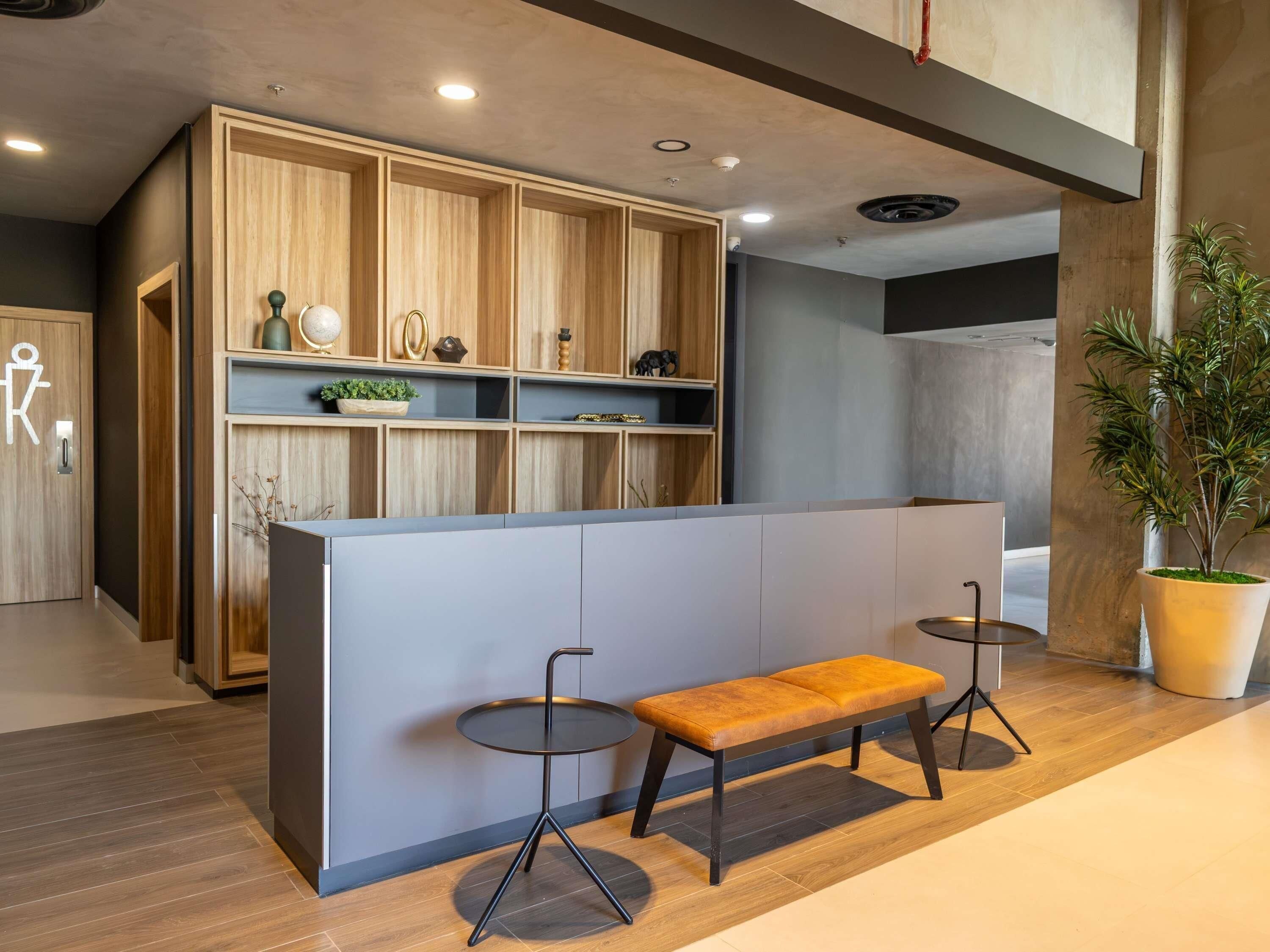 Un espace d’accueil comprenant un comptoir de réception en bois, deux petites tables rondes, un banc et une plante en pot.