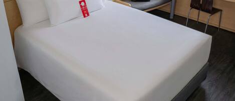 Habitación de hotel con una cama bien tendida, un escritorio con una silla, un teléfono y un bolso sobre el escritorio.