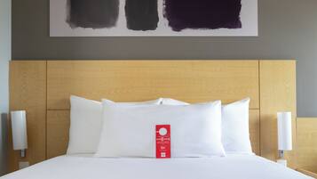 Habitación de hotel con una cama grande, ropa blanca, cabecera de madera y una obra de arte colgada en la pared.