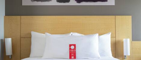 A hotel room with a large bed, white bedding, a wooden headboard, and a wall-mounted artwork.