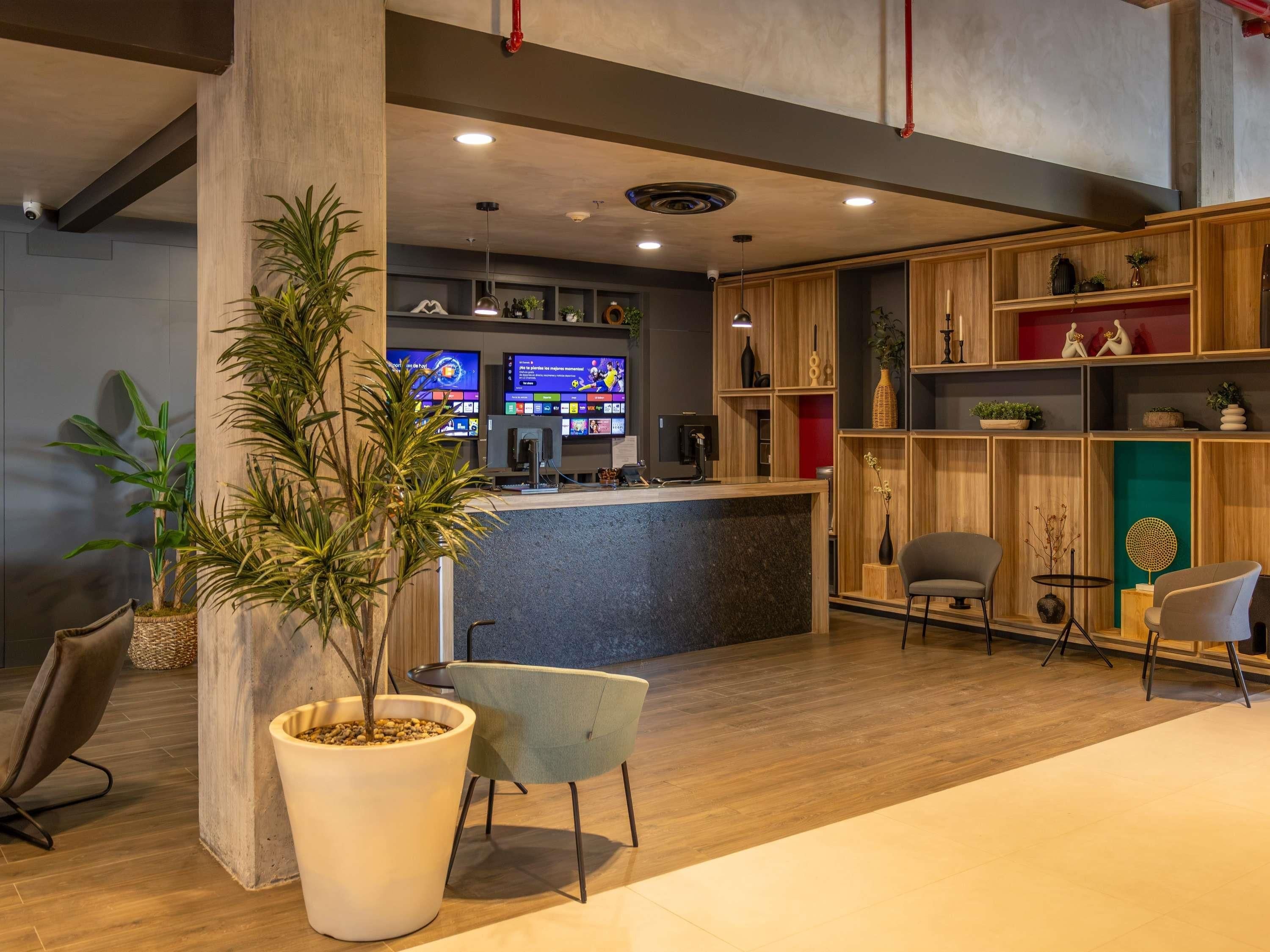 A modern reception area with a wooden reception desk, two televisions, and a large potted plant.
