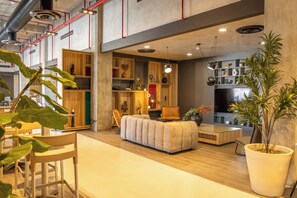 Una sala de estar moderna con un sofá, una mesa de centro y un televisor. Hay estanterías de madera con objetos decorativos y una planta grande en maceta.