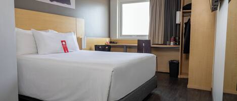 A hotel room with a bed, a window, a desk, and a wardrobe.