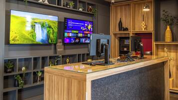 A reception area with a wooden reception desk, a flat-screen TV displaying a nature scene, a digital screen with various icons, and shelves with decorative items.