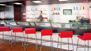 A modern bar area with red bar stools, a glass counter, and shelves with colorful bottles. - ibis Hermosillo (Hermosillo)