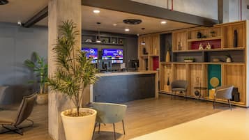 A modern reception area with a wooden reception desk, two chairs, a large potted plant, and a wall-mounted TV.