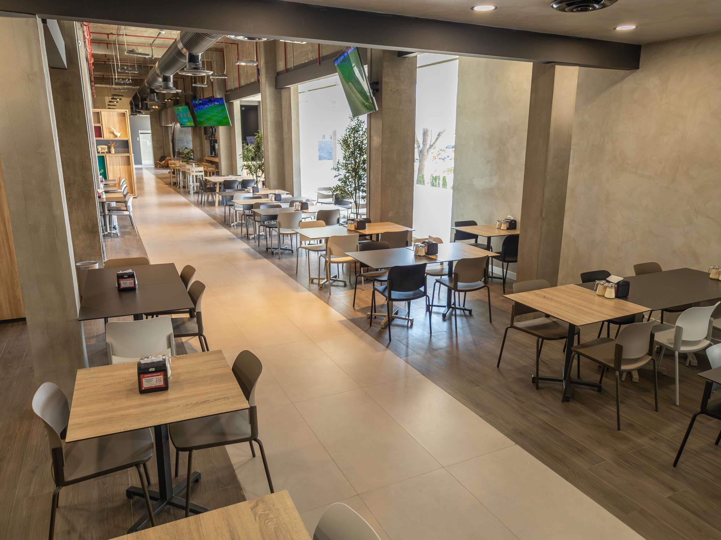 A spacious indoor area with multiple tables and chairs, a long corridor, and large windows allowing natural light.