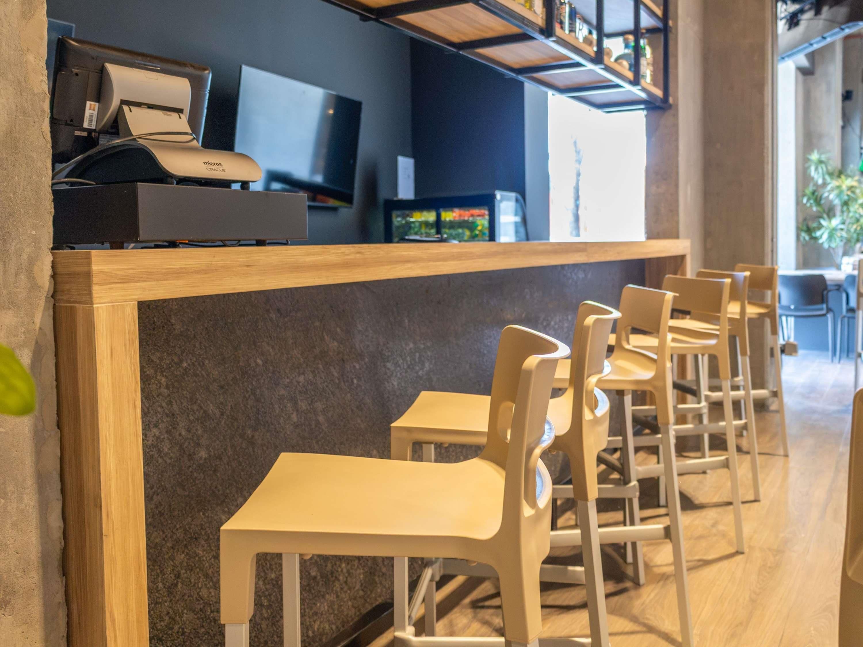 Interior de una cafetería con mostrador, sillas y televisor.