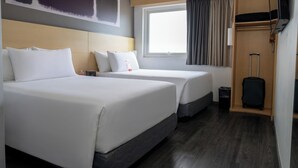 A hotel room with two beds, a window with curtains, a TV, and a suitcase storage area. - ibis Hermosillo (Hermosillo)