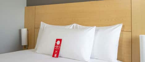 Una cama bien hecha con ropa blanca y almohadas, un cabecero de madera y una lámpara de pared.