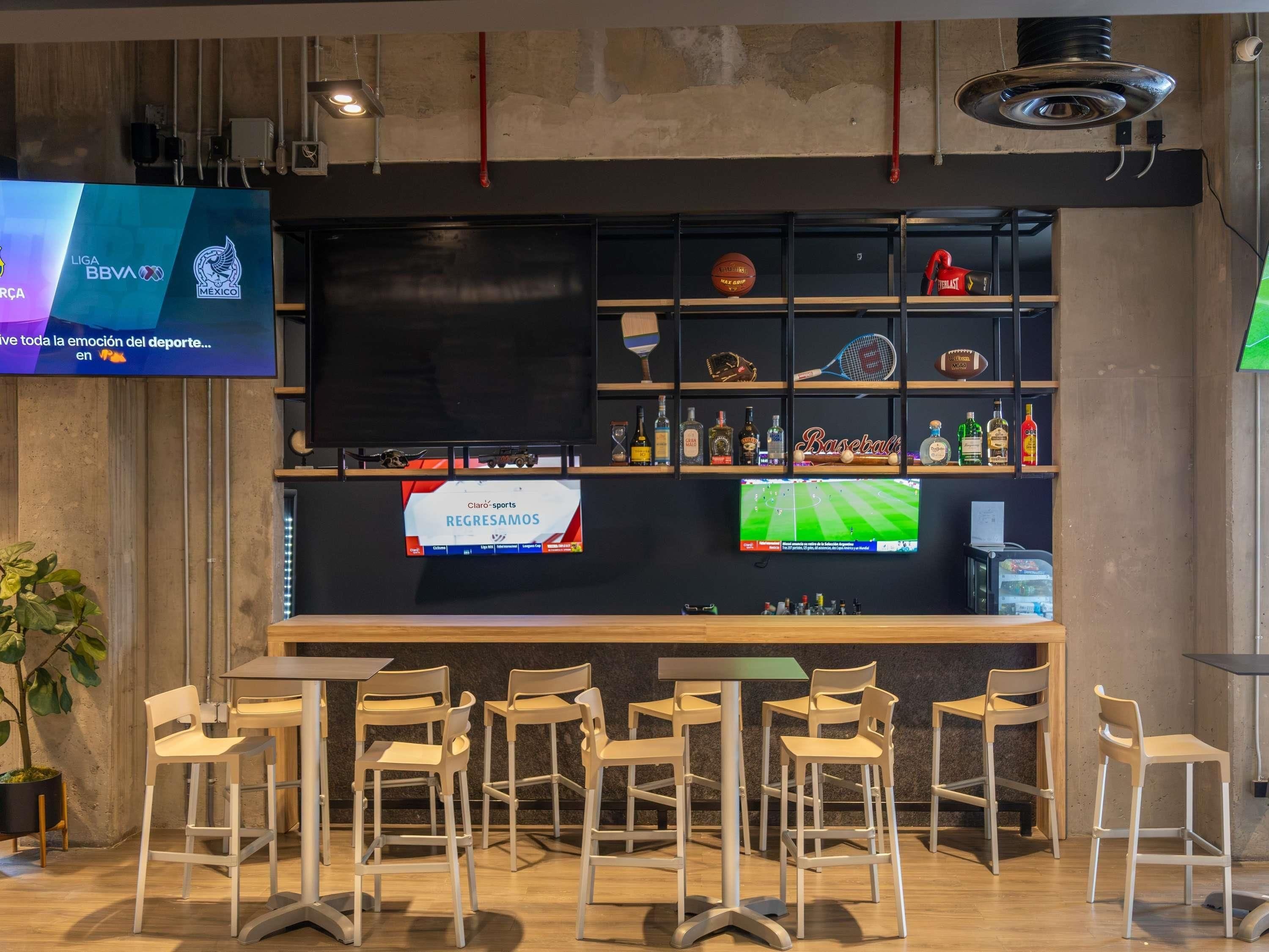 A sports bar with a large TV screen displaying sports content, a bar area with stools, and shelves with sports memorabilia and bottles.