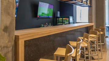 A bar area with a counter, chairs, a television screen, and shelves with bottles.