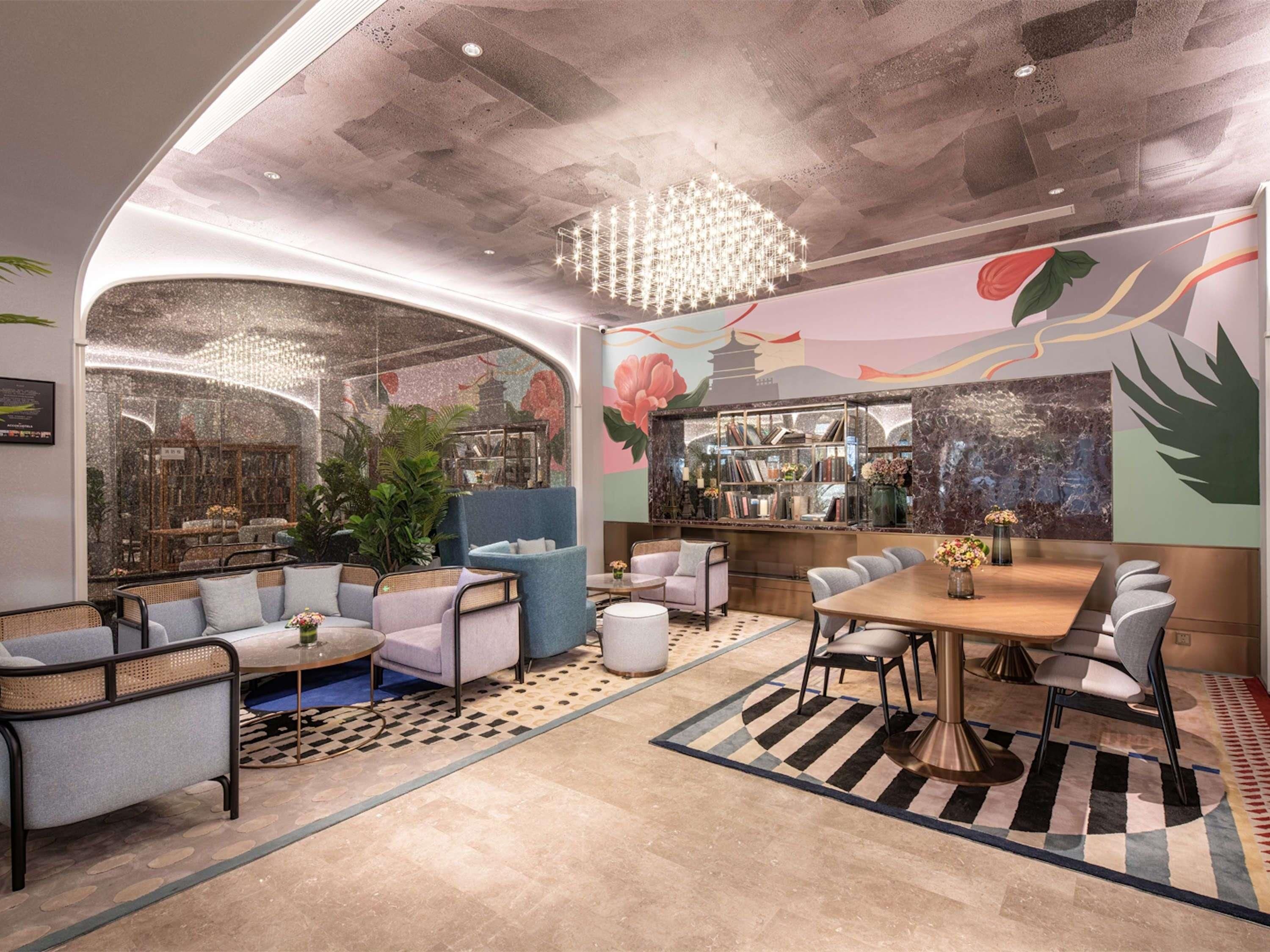 A modern interior with a curved ceiling, a chandelier, a seating area with sofas and chairs, a bar with bookshelves, and a mural on the wall.