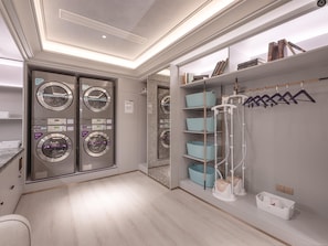 Un cuarto de lavandería con cuatro lavadoras, un tendedero y un estante con ropa colgada.