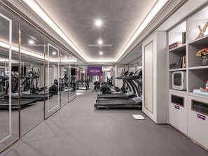 A gym with treadmills, weights, and exercise machines, a mirrored wall, and a sign for Mercure Hotels.