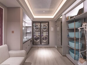 Un lavadero de hotel con cuatro lavadoras apiladas, un sofá y estantes con cajas de almacenamiento.