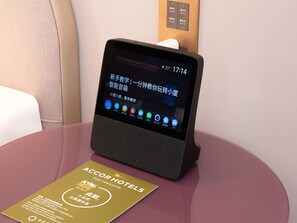 Una tableta mostrando una interfaz digital con íconos, un cartel de habitación de hotel y un panel de control en la pared.