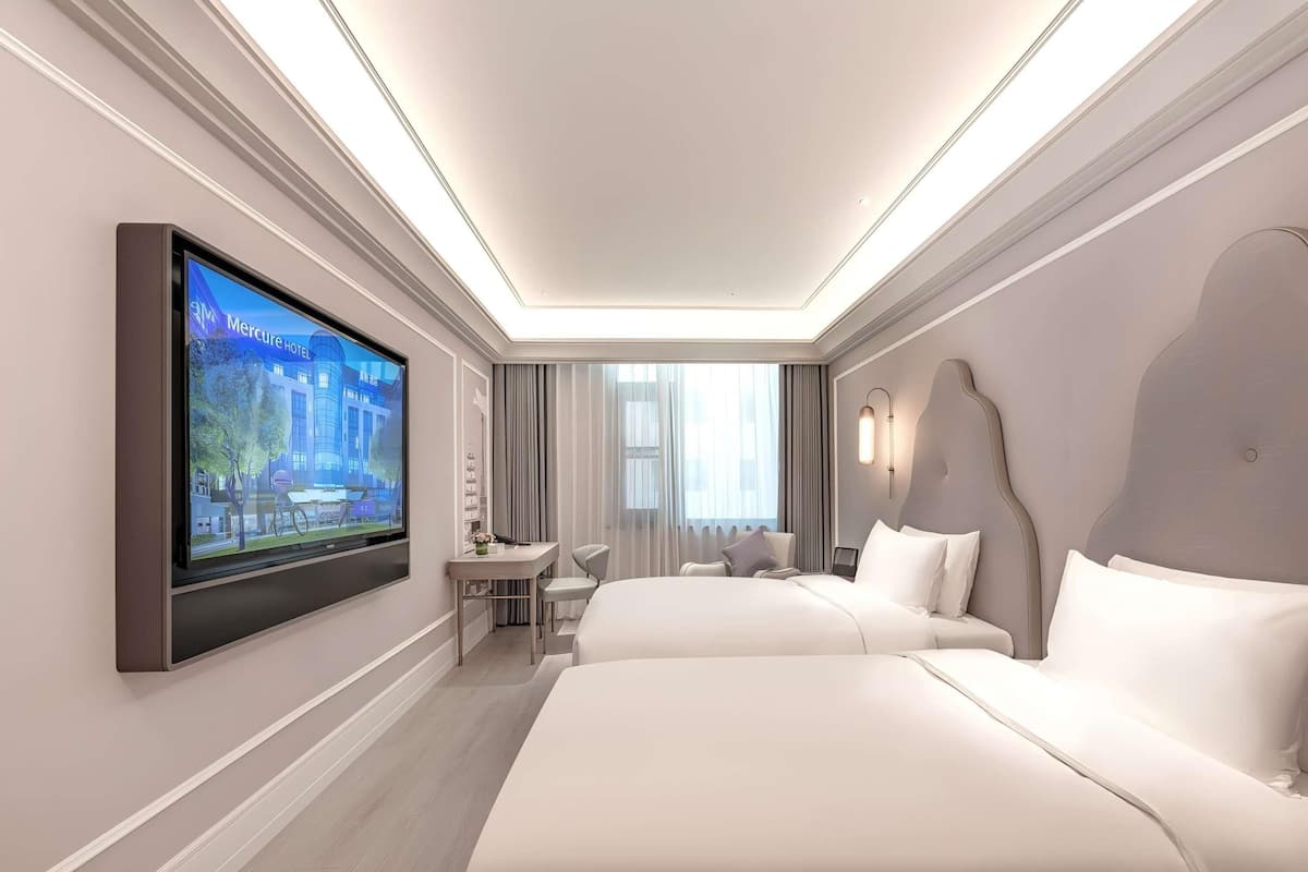 Habitación de hotel moderna con una televisión de pantalla plana grande, dos camas, un escritorio y una silla.