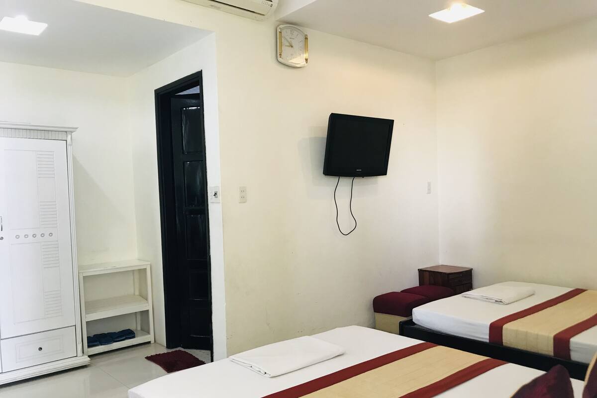 A hotel room with two beds, a TV mounted on the wall, a wardrobe, and a small table.