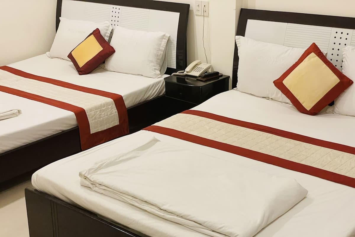 A hotel room with two beds, each with a red and white bedspread, a telephone on a bedside table, and a folded white towel on the floor.