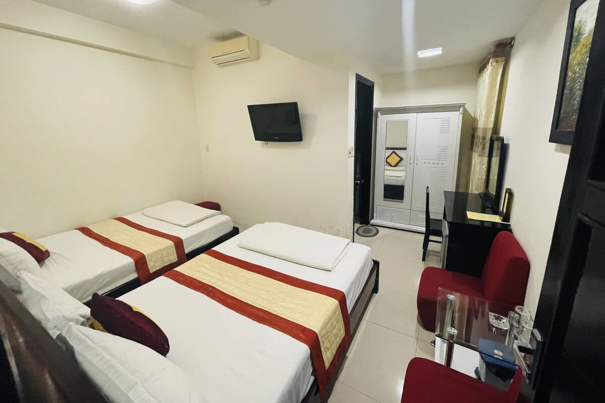 A hotel room with two beds, a TV, a wardrobe, and a small table with chairs.