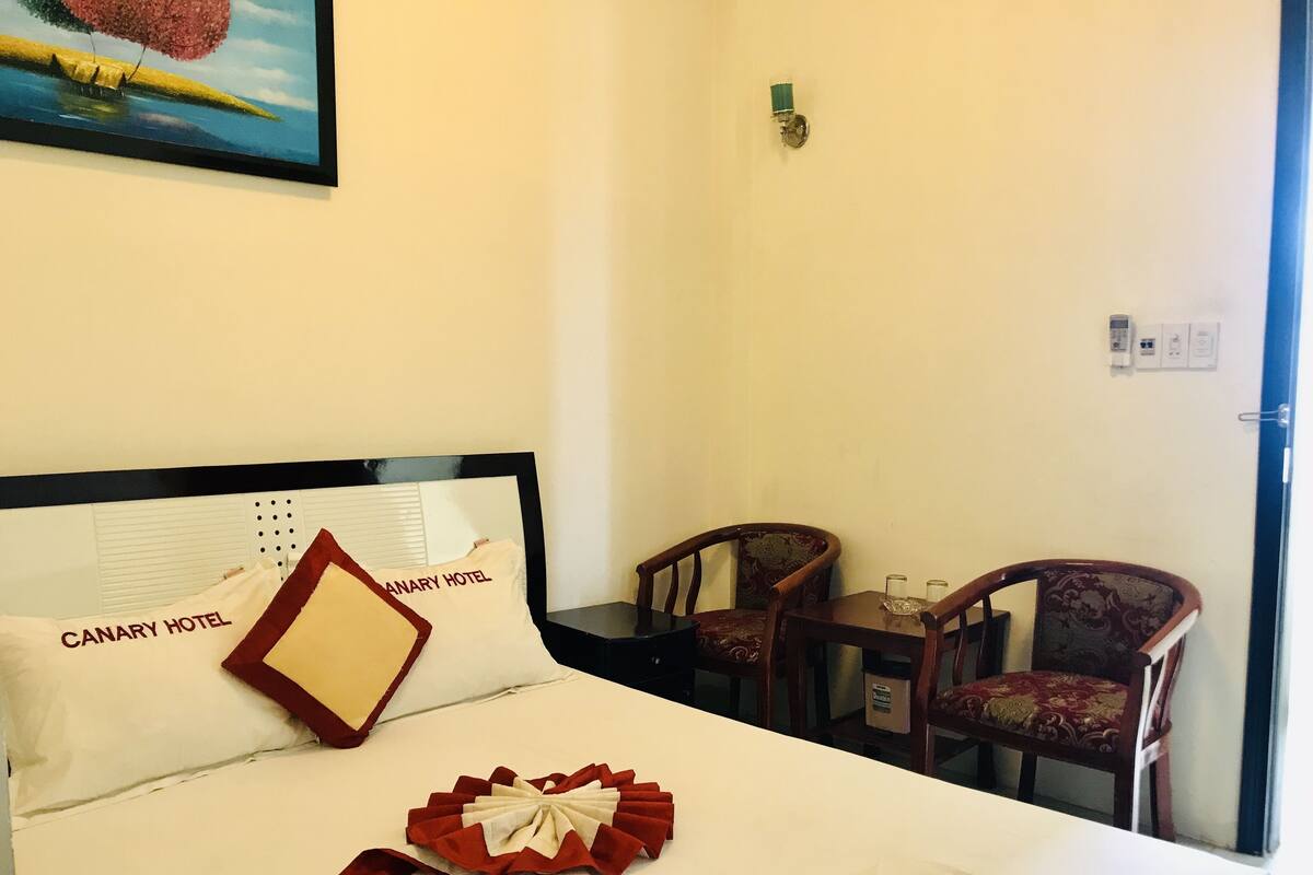 A hotel room with a bed, two chairs, a small table, and a painting on the wall.