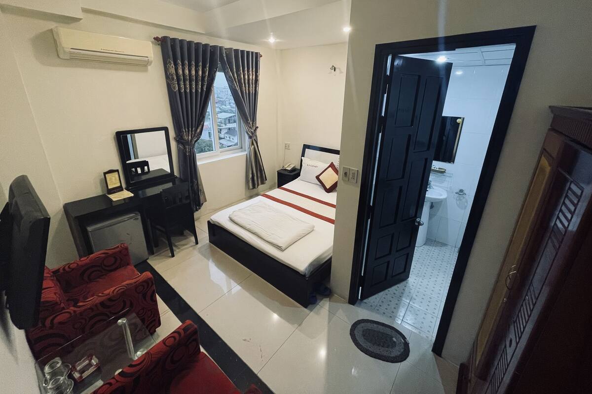 A hotel room with a bed, desk, chair, and a window with curtains.