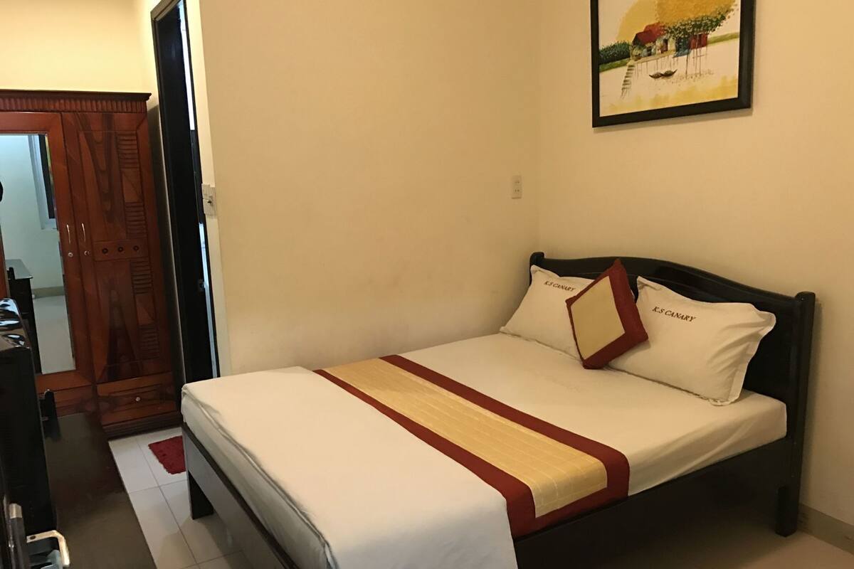 A hotel room with a bed, a wooden wardrobe, and a painting on the wall.