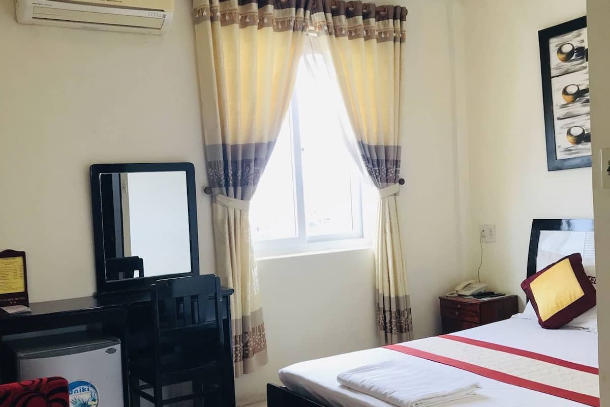 A hotel room with a bed, desk, chair, and a window with curtains.