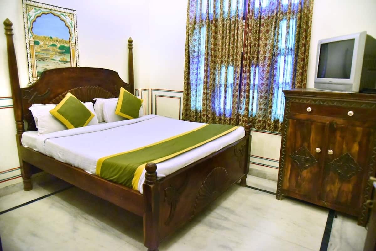 A neatly made bed with a wooden frame, a green and white bedspread, and two pillows. There is a television on a wooden cabinet to the right.