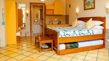 A hotel room with a wooden bed, a small table, a bench, a kitchen area, and a bathroom.