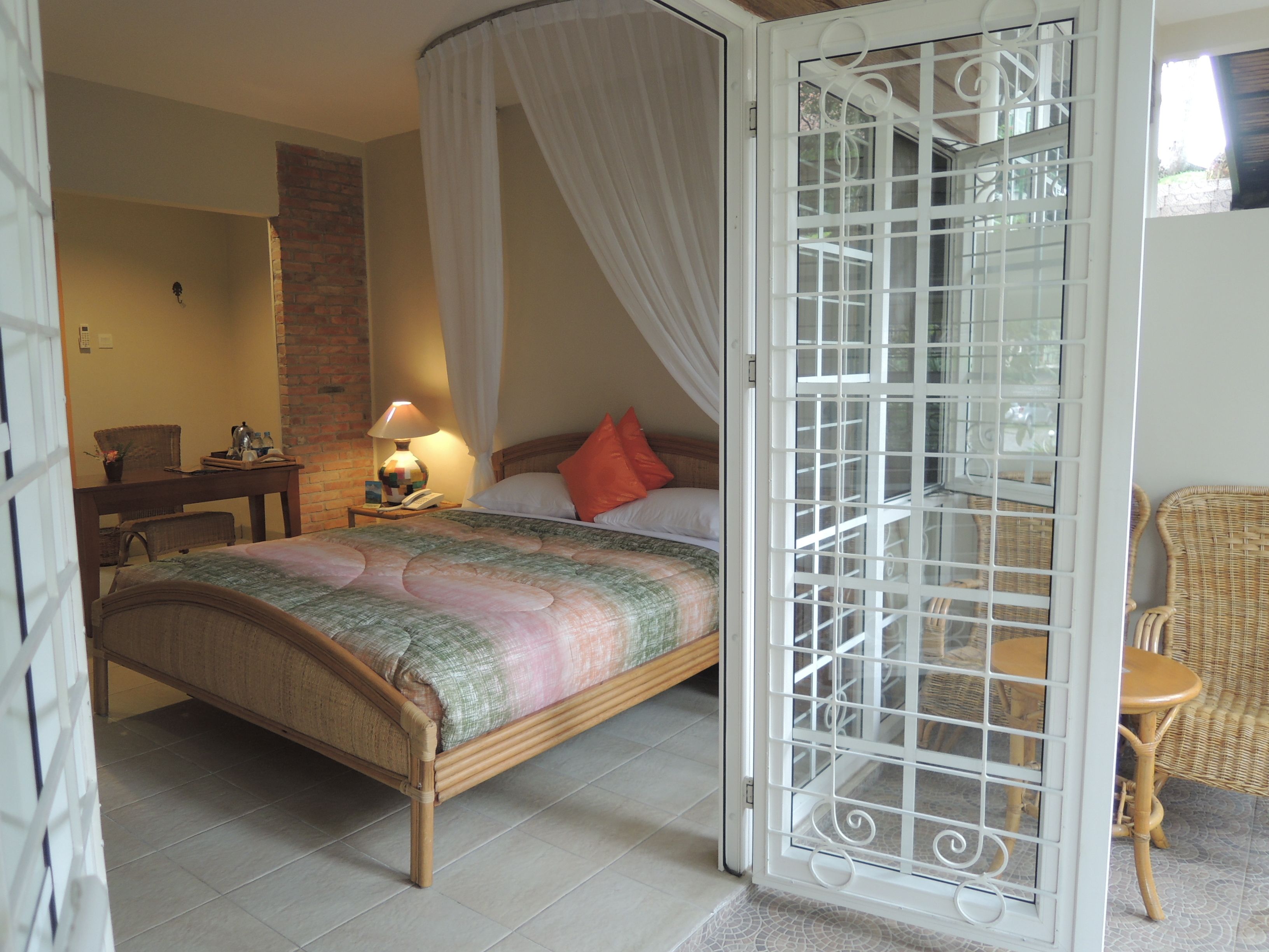 A bedroom with a bed, a nightstand, a lamp, a chair, and a window with a metal screen.