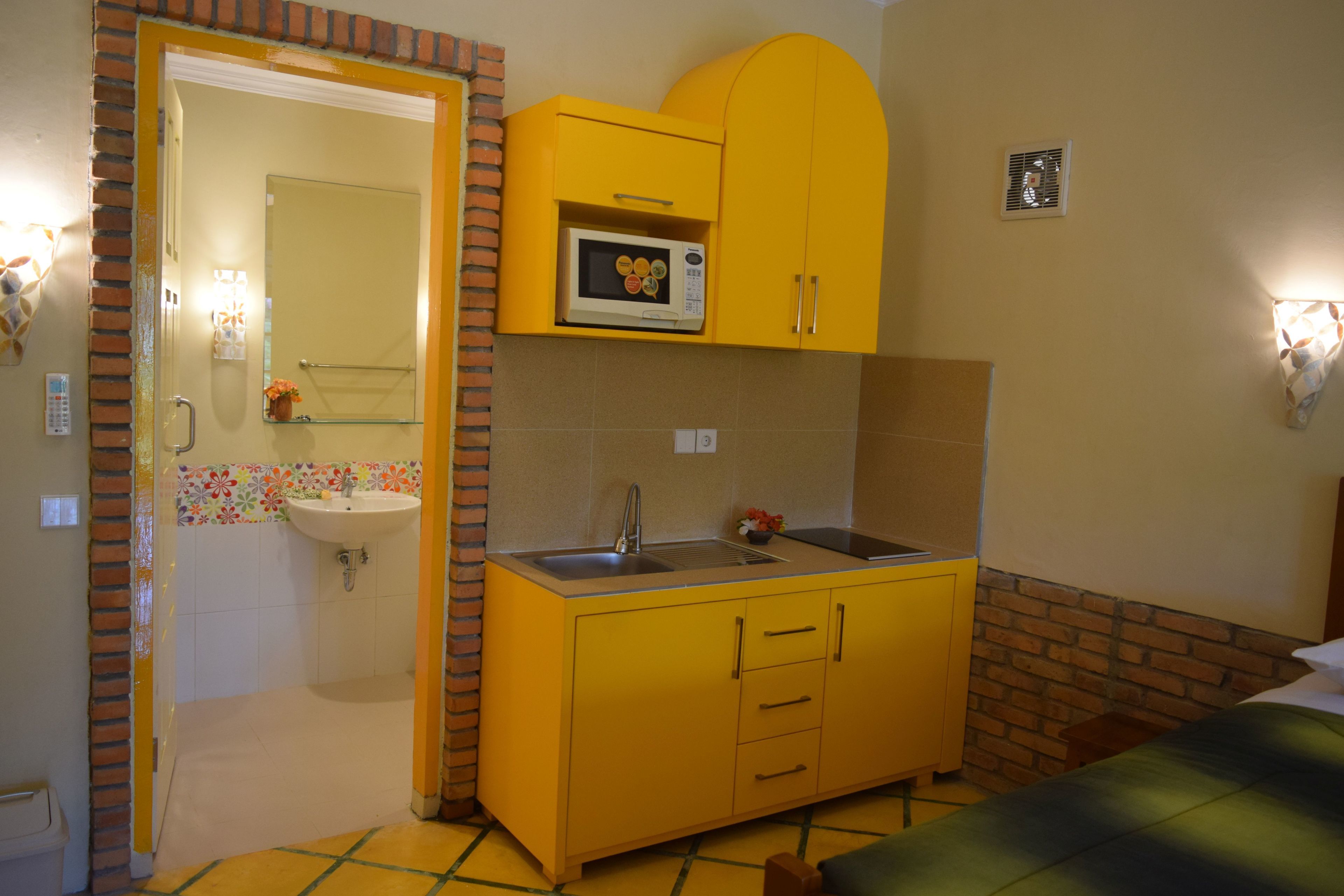 A compact room with a yellow kitchenette, a sink, and a microwave.
