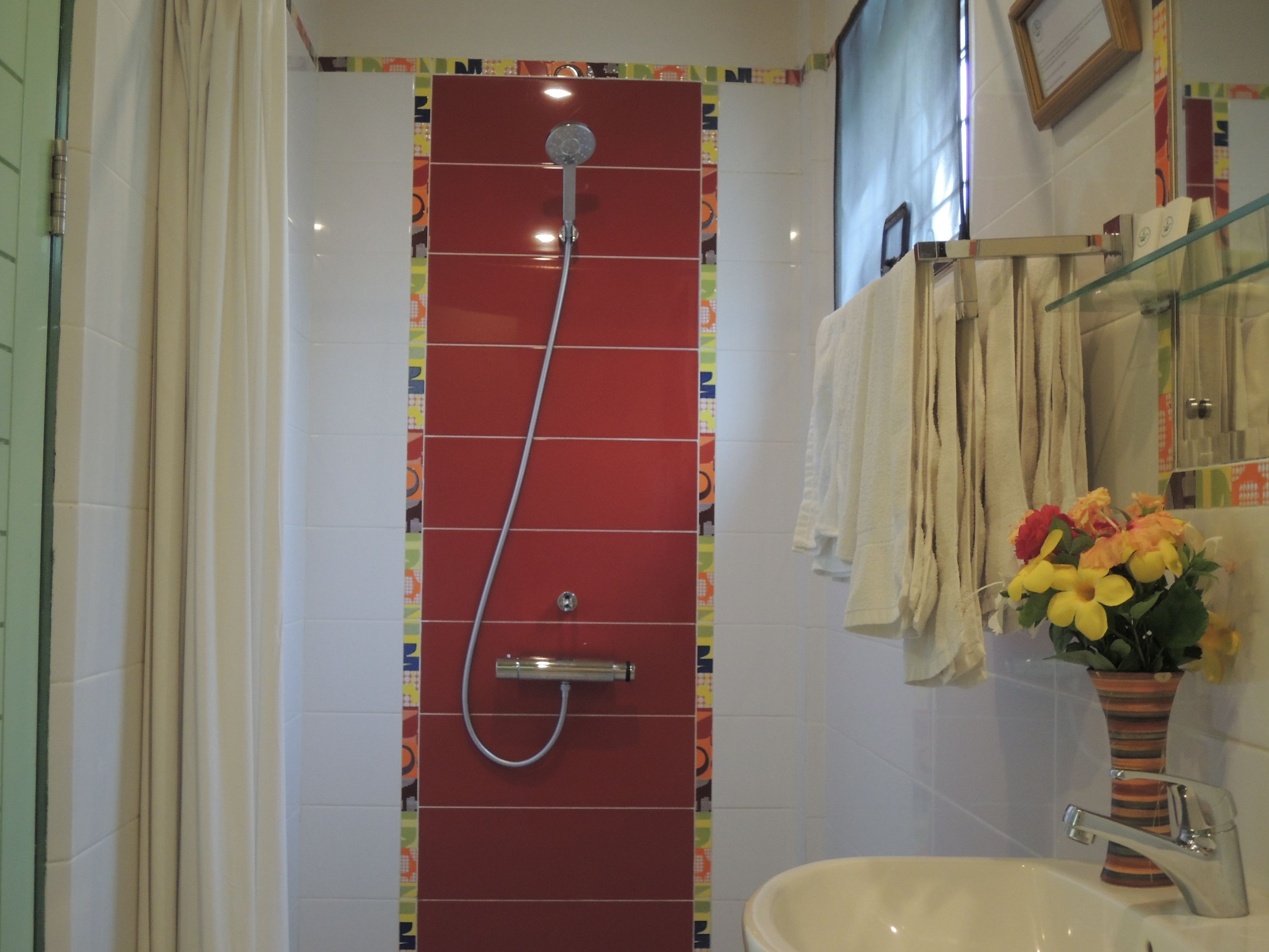 A bathroom with a red shower enclosure, a white sink, and a vase with flowers.