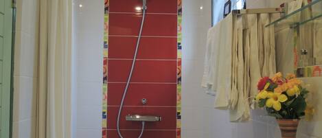 A bathroom with a red shower enclosure, a white sink, and a vase with flowers.