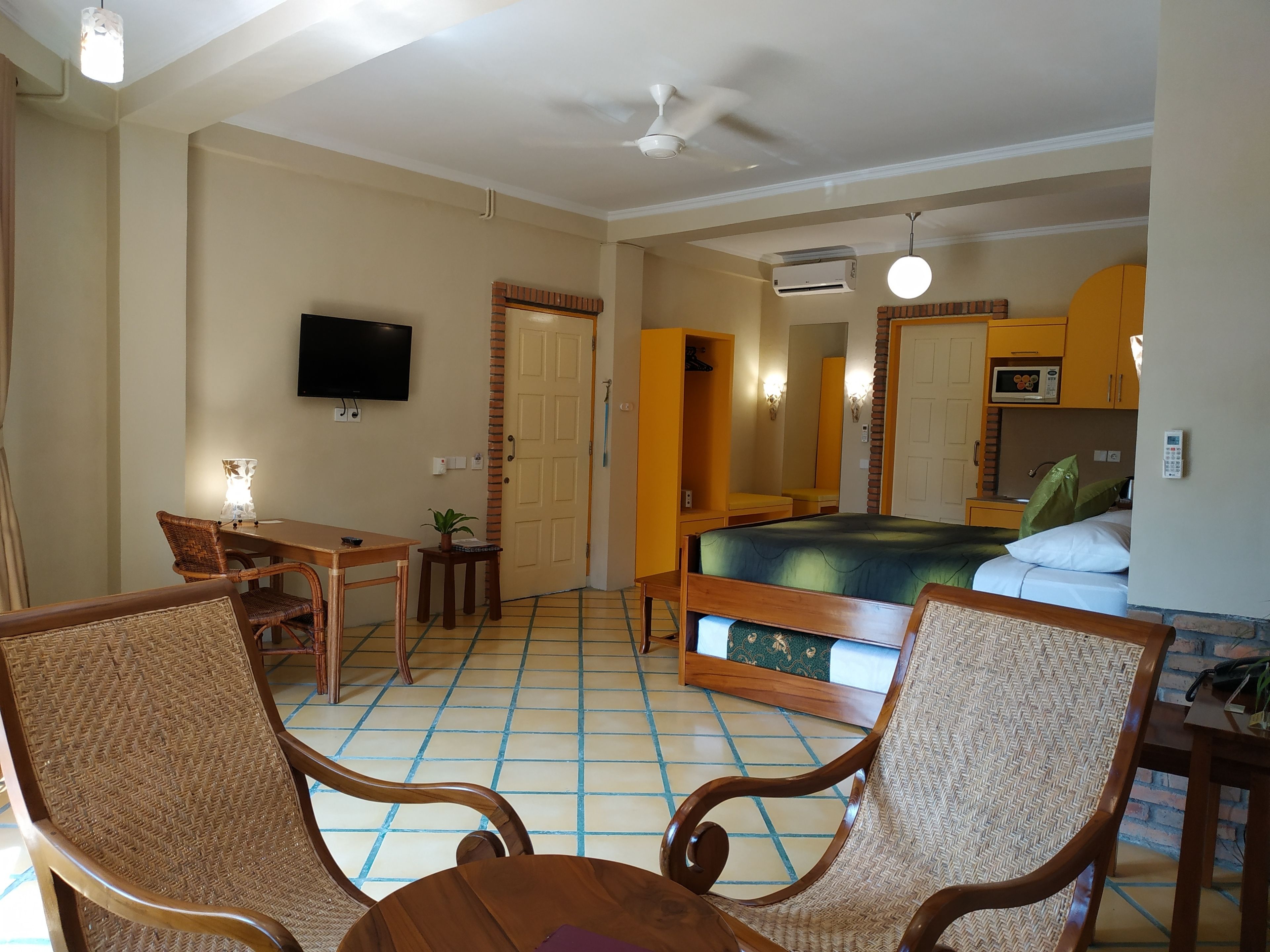 Una habitación de hotel con una cama, un escritorio, dos sillas, un televisor y un ventilador de techo.